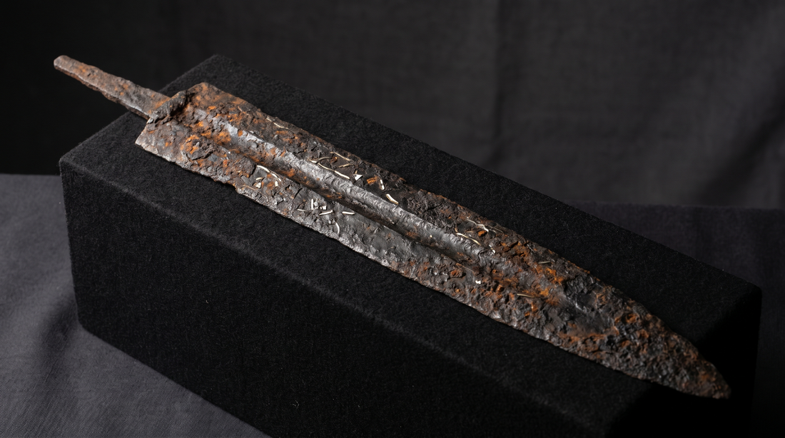 Heavily corroded iron langseax blade with its handle long rotted away, under raking museum light