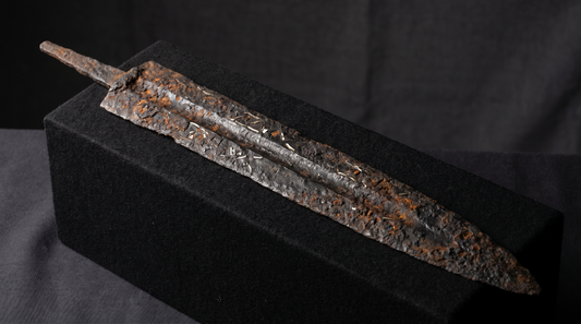 Heavily corroded iron langseax blade with its handle long rotted away, under raking museum light