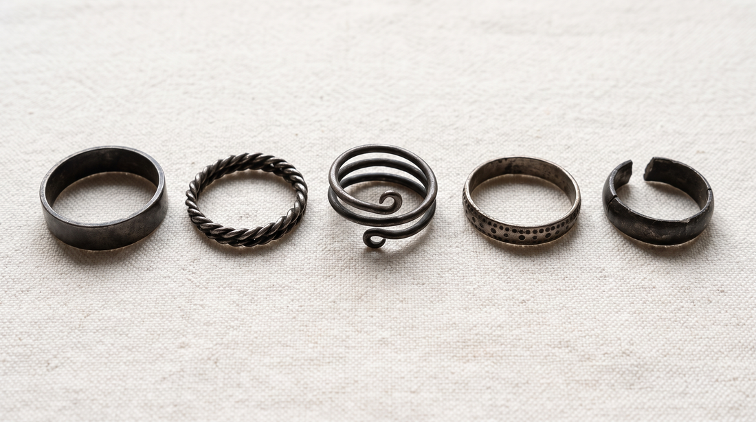 Five plain Viking-age silver finger rings on linen: a flat band, a twisted wire ring, a three-coil spiral, a band with punched dots, and a cut ring fragment