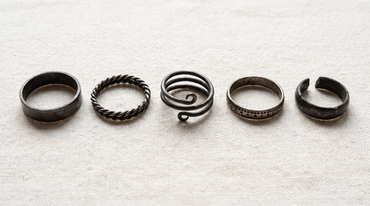 Five plain Viking-age silver finger rings on linen: a flat band, a twisted wire ring, a three-coil spiral, a band with punched dots, and a cut ring fragment