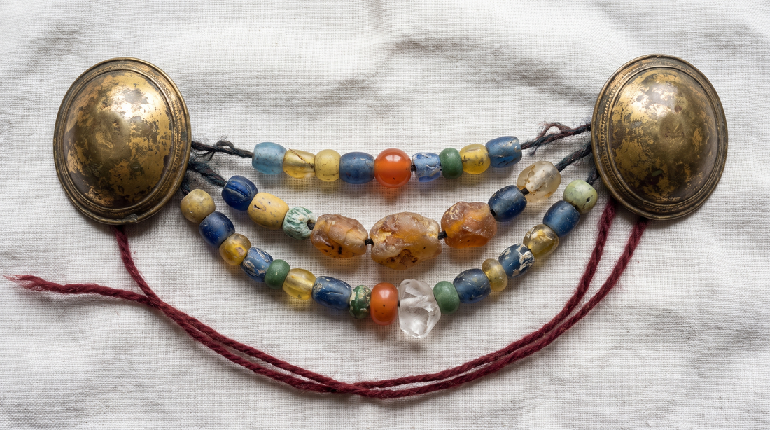 A Viking-age bead festoon on linen: two oval bronze tortoise brooches with three uneven strands of glass, amber, carnelian and rock crystal beads strung between them