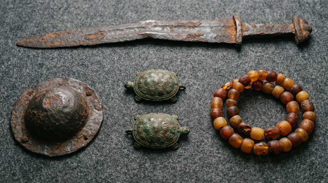 Viking Age grave goods on conservation felt: a corroded iron sword, a shield boss, two oval bronze tortoise brooches and a string of amber beads
