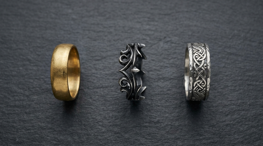 Three wedding bands on slate, a plain gold band, a blackened gothic ring and a Norse knotwork band