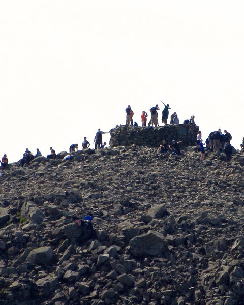 Walkers crowding the rocky summit of Scafell Pike in the Lake District, around the stone summit cairn (photo: Peer Lawther, CC BY 2.0)