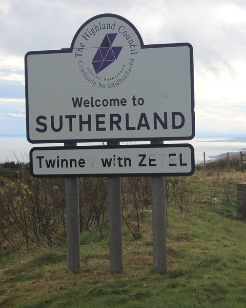 The Highland Council's Welcome to Sutherland road sign at the Ord of Caithness, on a grassy slope above the sea (photo: Roger Davies, CC BY-SA 2.0)
