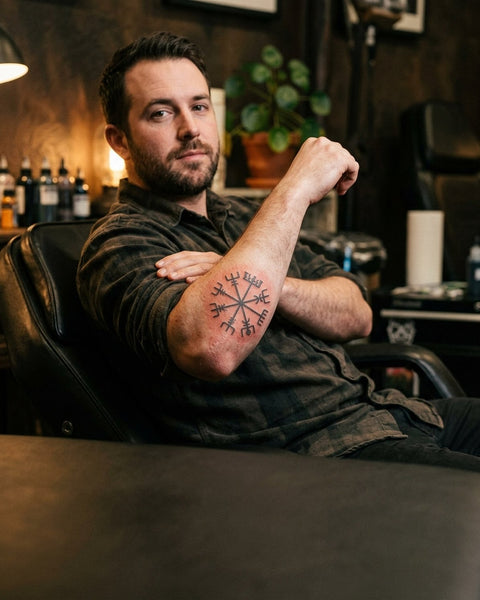 A man in a tattoo studio shows a Norse-style symbol tattooed on his forearm