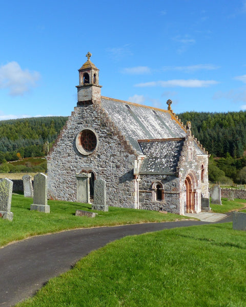 A small stone country kirk with a bellcote and a round window, gravestones on the grass and a path curving past, under a blue sky at Cranshaws in the Scottish Borders (photograph)