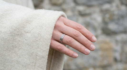 A woman's hand from a wool cloak sleeve wearing a slim silver band with fine knotwork