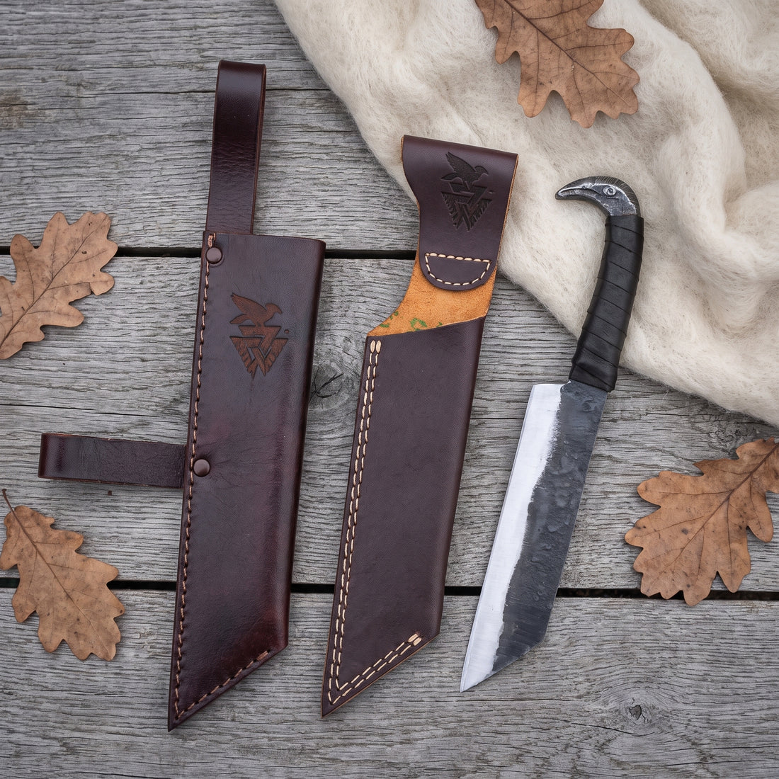 Broken-Back Viking seax knife laid out with both leather sheaths — the belt sheath with riveted loop and the plain slip sheath — on weathered grey planks