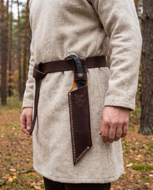 Broken-Back Viking seax knife worn on the hip in its belt sheath, hanging from the riveted loop over a wool tunic in the forest