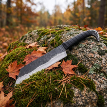Broken-Back Viking seax knife laid across moss and autumn leaves on a granite boulder, forge-textured blade meeting the bright ground bevel