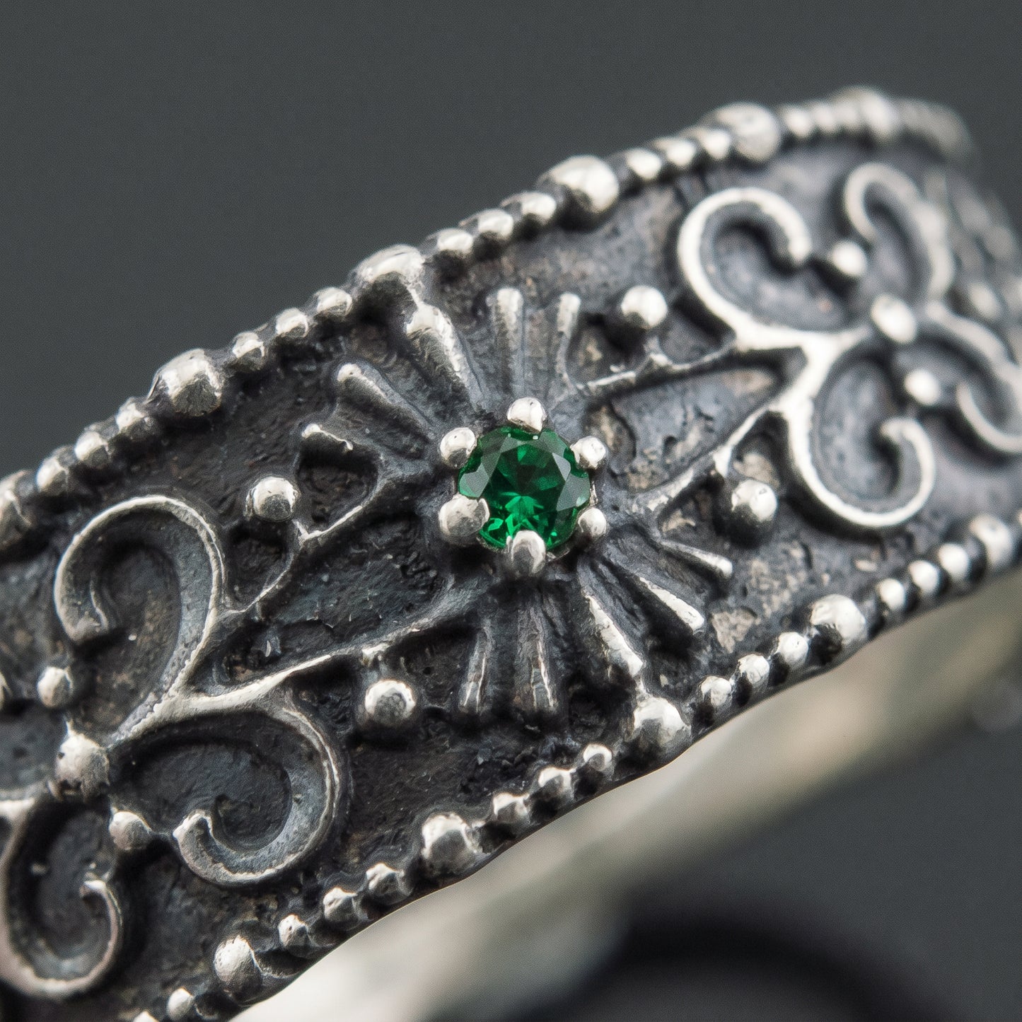 Macro of the green gem in its radiating panel and the beaded silver filigree