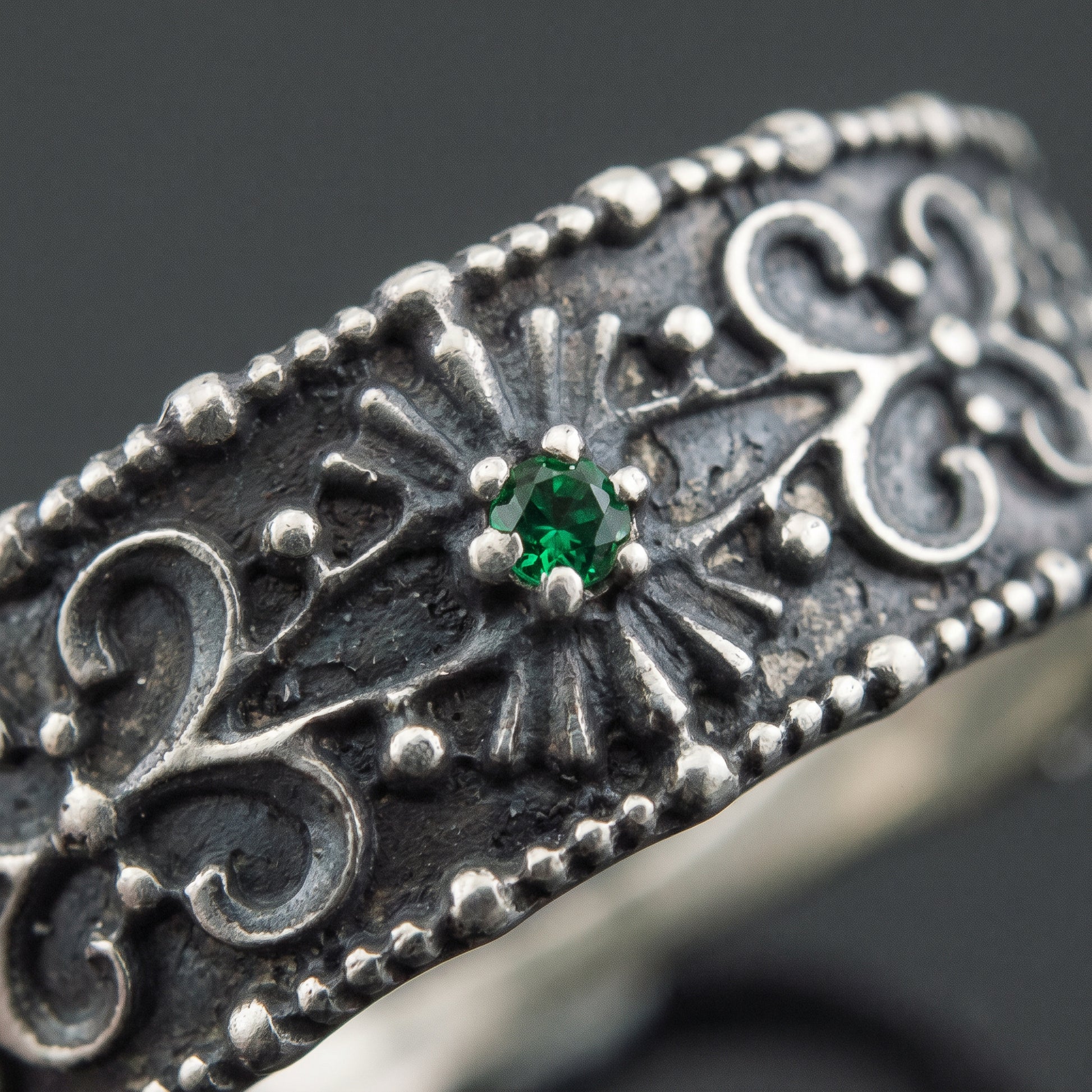 Macro of the green gem in its radiating panel and the beaded silver filigree