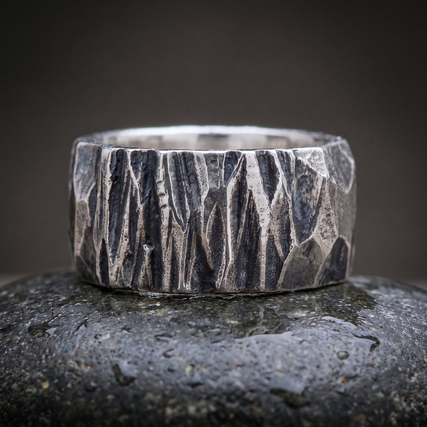 Wide hand-forged 925 silver band seen front on, chisel-faceted oxidised surface
