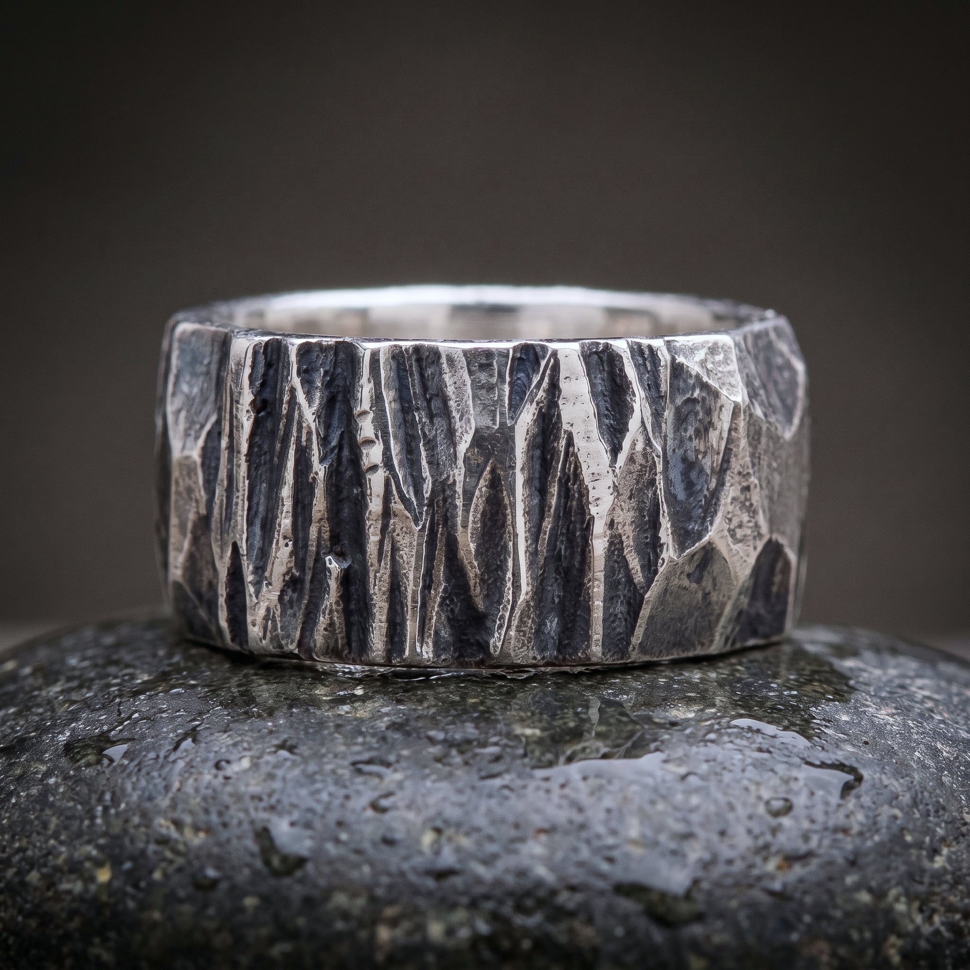 Wide hand-forged 925 silver band seen front on, chisel-faceted oxidised surface