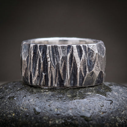 Wide hand-forged 925 silver band seen front on, chisel-faceted oxidised surface