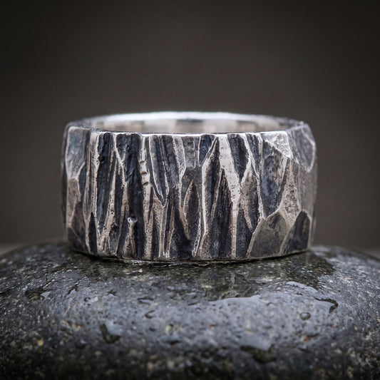 Wide hand-forged 925 silver band seen front on, chisel-faceted oxidised surface