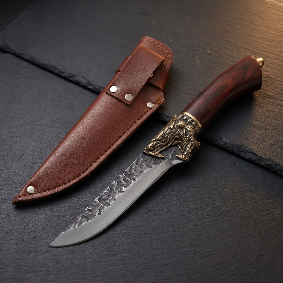 Fenrir hand-forged boning knife with hammered 7-inch blade, cast brass bolster and rosewood handle, beside its riveted leather sheath