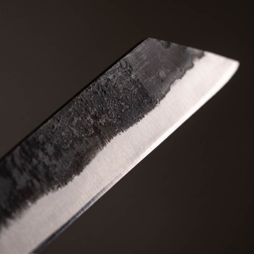 Macro of the hand-forged carbon steel blade of the Broken-Back seax showing forge skin meeting the bright ground bevel