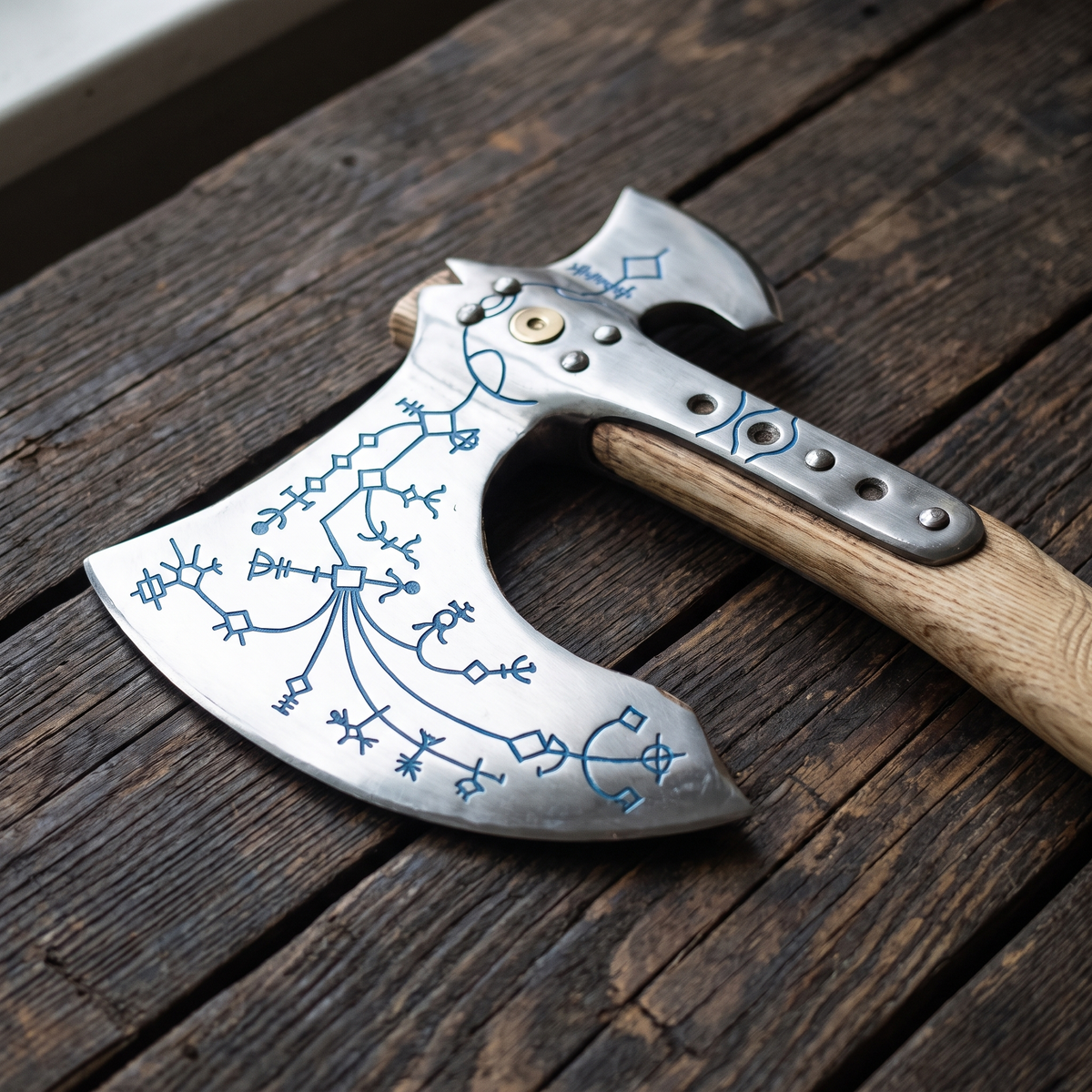 Close-up of the engraved axe head: blue branching rune-style symbols, riveted steel langet and brass-coloured boss
