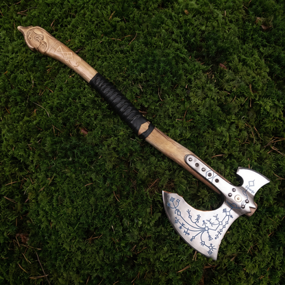 Full-length view of the hand-forged Kratos axe, a Viking-style engraved axe, lying on green moss