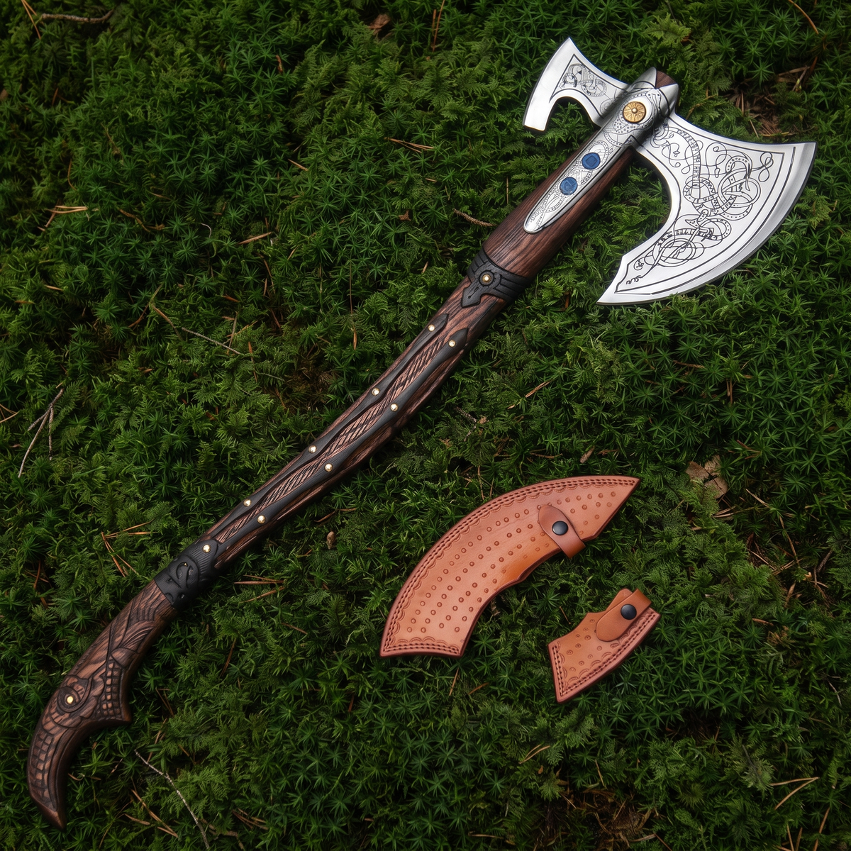 Leviathan Axe with engraved high-carbon steel head and carved wooden handle, shown with its leather sheath on moss