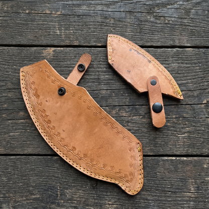 Two tan leather blade covers for the axe, stitched edges with a stamped border and snap straps
