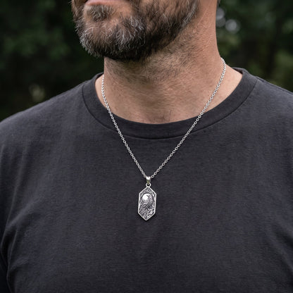 Man wearing the Norse raven pendant on a thin silver chain over a charcoal t-shirt, shown at true size