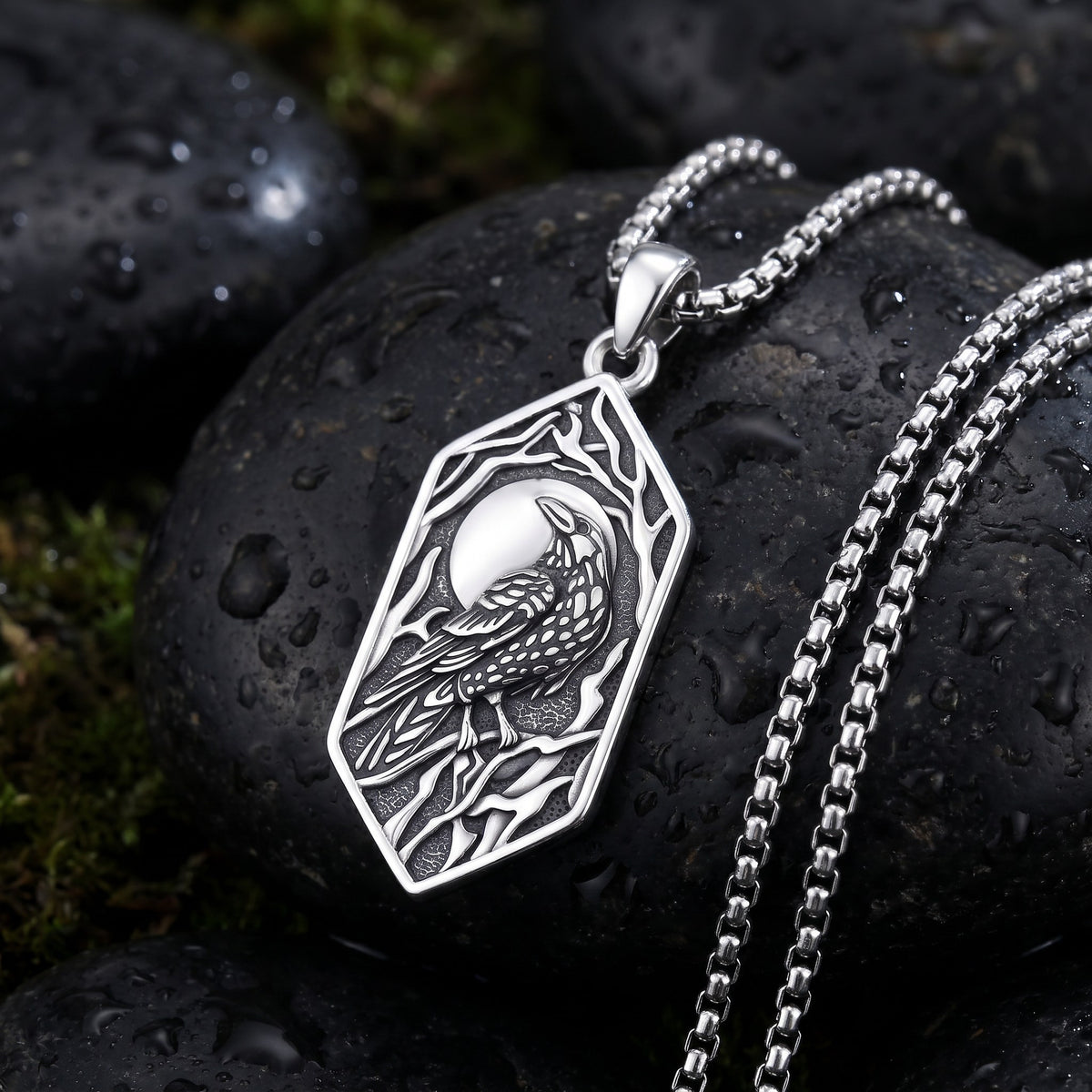Raven and moon pendant on the 24 inch stainless steel box chain, laid on a wet dark river stone