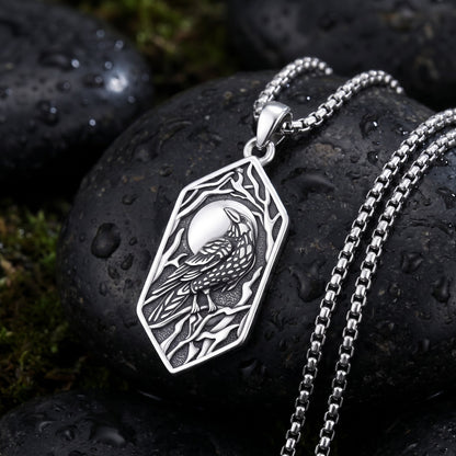 Raven and moon pendant on the 24 inch stainless steel box chain, laid on a wet dark river stone