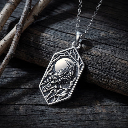 Oxidized sterling silver raven necklace resting on dark weathered timber in cold moonlit light