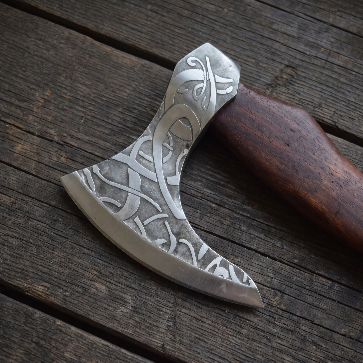 Close-up of the bearded axe head: pale interlaced knotwork acid-etched on a grey steel ground, with a bright cutting edge