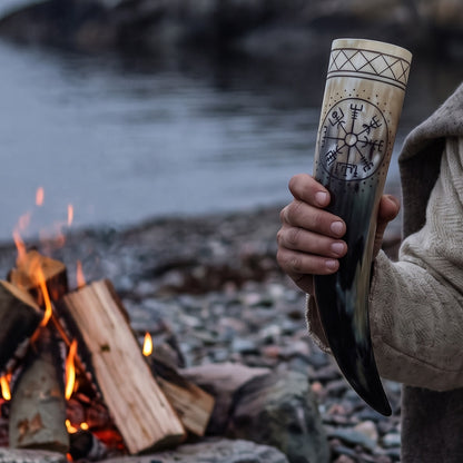 Hand holding the Vegvisir drinking horn by a fire on a stony shore