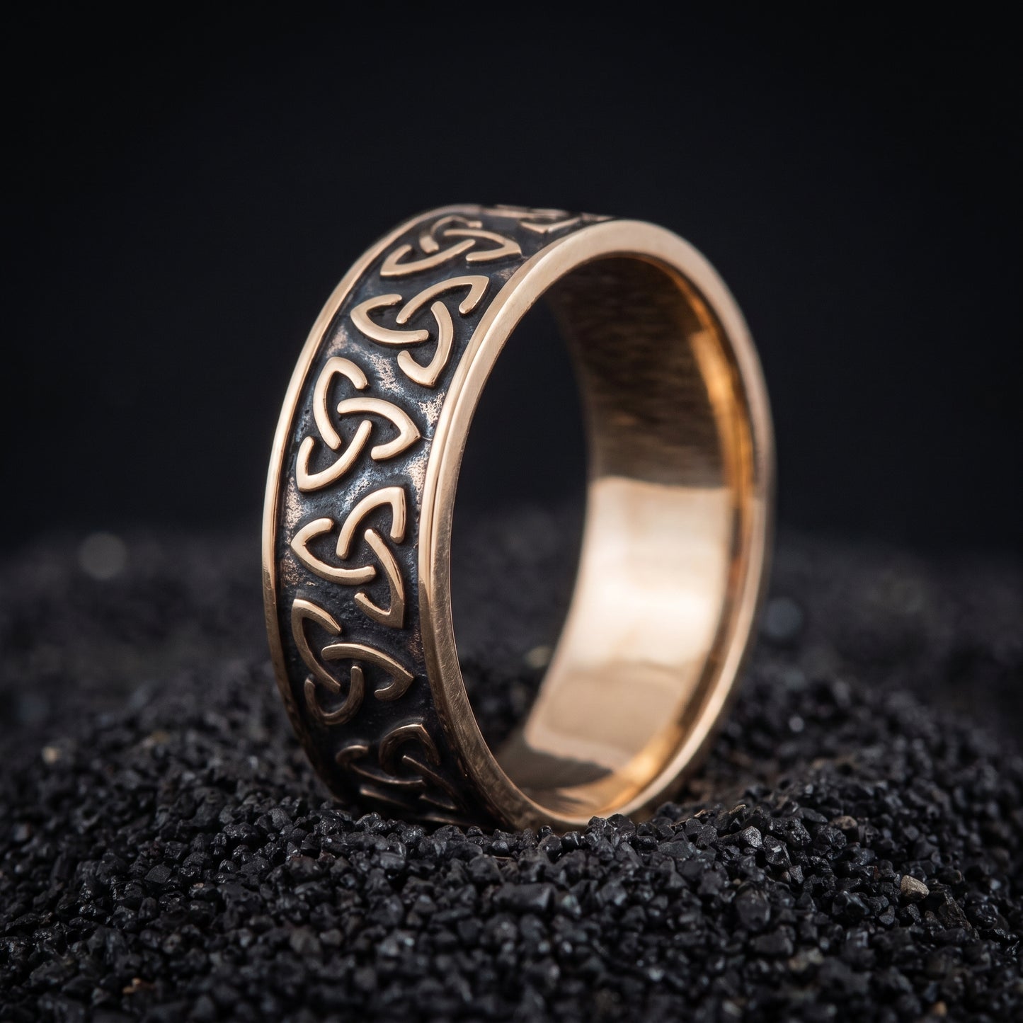 Bronze Viking wedding ring with a chain of triquetra knots on black volcanic sand