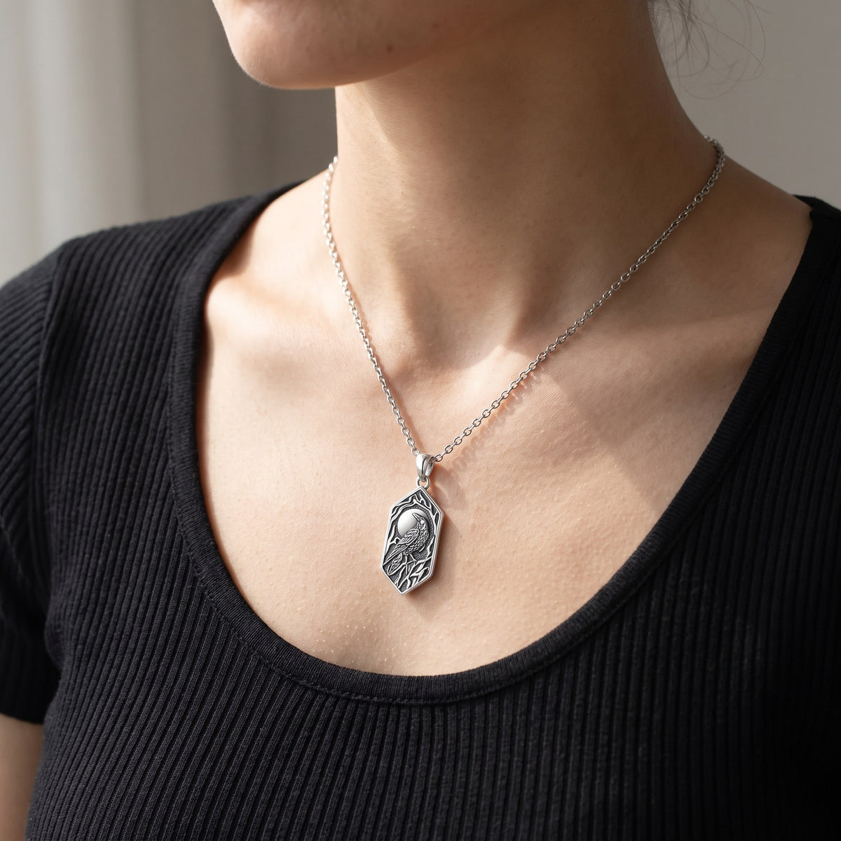 Woman wearing the raven and moon sterling silver necklace on a thin cable chain over a black top