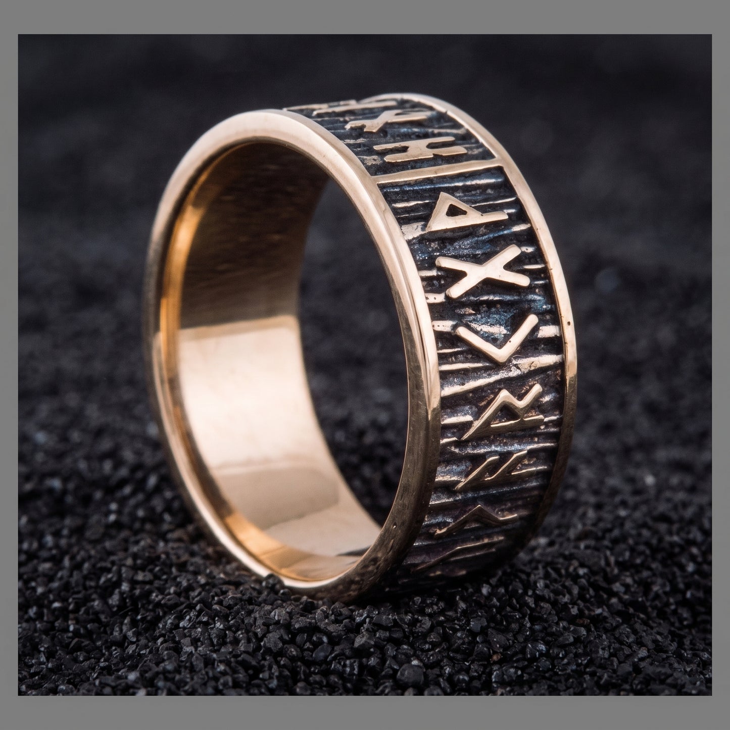 Elder Futhark runes bronze Viking ring with wide polished rims on black volcanic sand