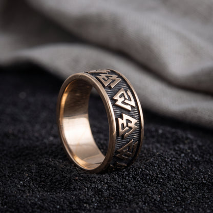 Handmade bronze Valknut Viking ring resting on black sand beside undyed grey linen