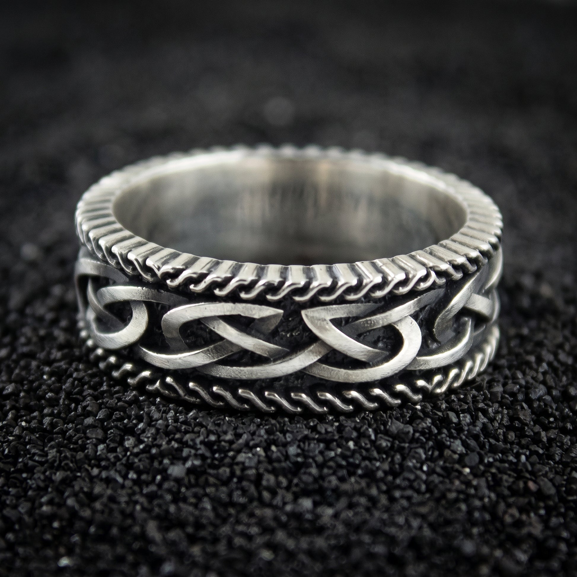 Norse knotwork Viking wedding ring in 925 sterling silver, twisted rope borders, on black volcanic sand