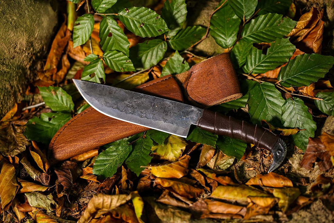Viking seax knife with forge-textured carbon steel blade lying on autumn leaves beside its leather sheath