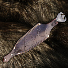 Close-up of the hand-tooled ornament and brass rivets on the Viking dagger's leather sheath, resting on fur