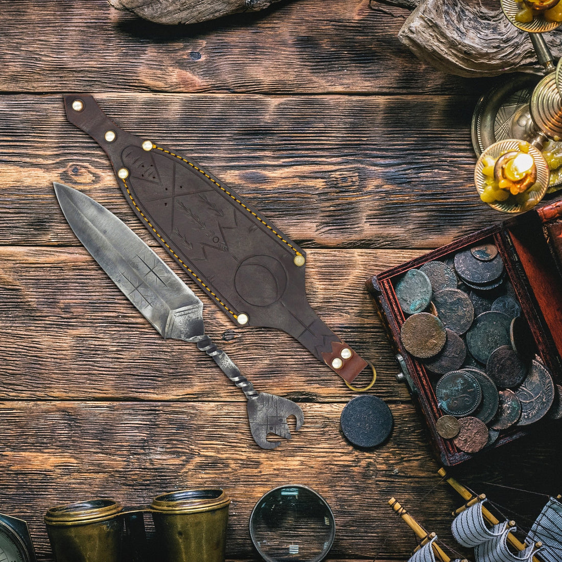 Hand-forged Norse dagger and leather sheath laid on weathered wood beside a chest of old coins