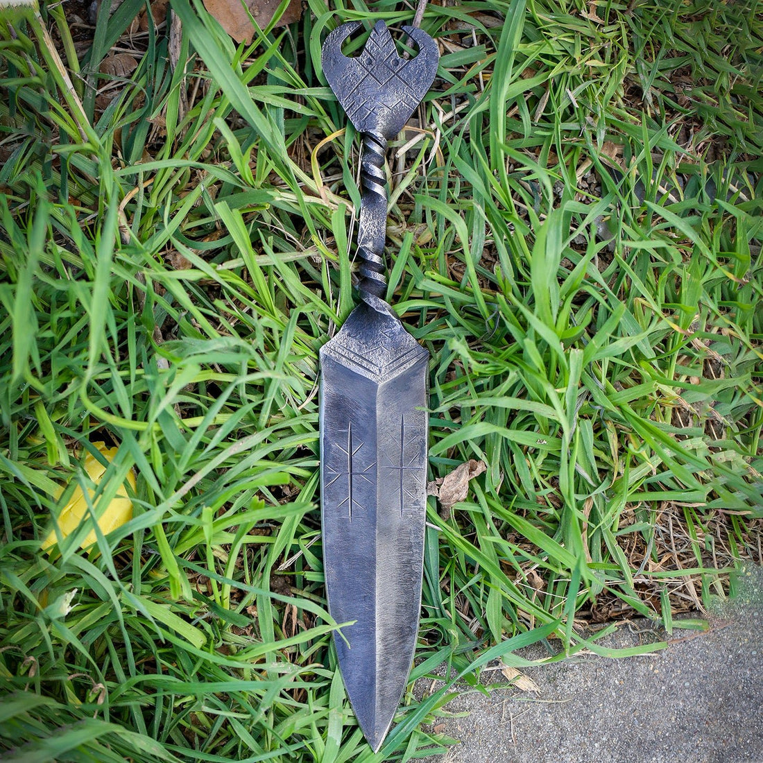 Viking dagger lying in grass, showing the twisted steel grip and flat forged pommel