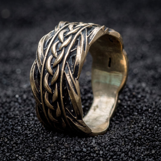 Bronze Viking wedding ring with woven Scandinavian ornament on black volcanic sand
