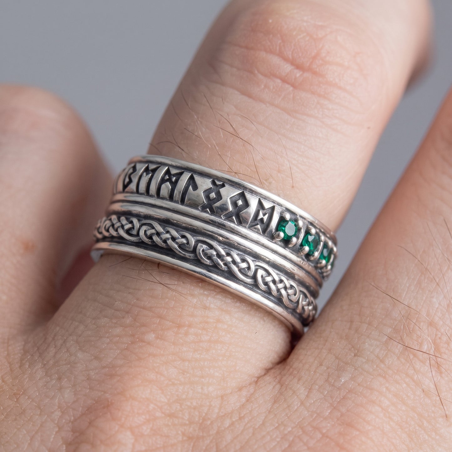 Silver Viking wedding ring with runes and green cubic zirconia worn on a finger