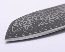 Close-up of Huginn and Muninn etched in interlaced Norse ornament across the darkened carbon steel blade